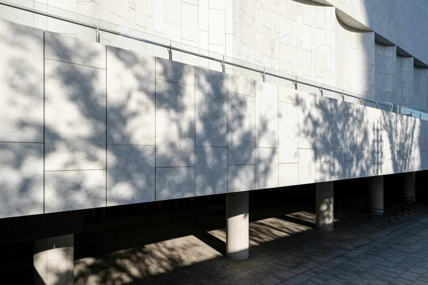 A stone-clad facade patterned with dappled tree shadow above a colonnade