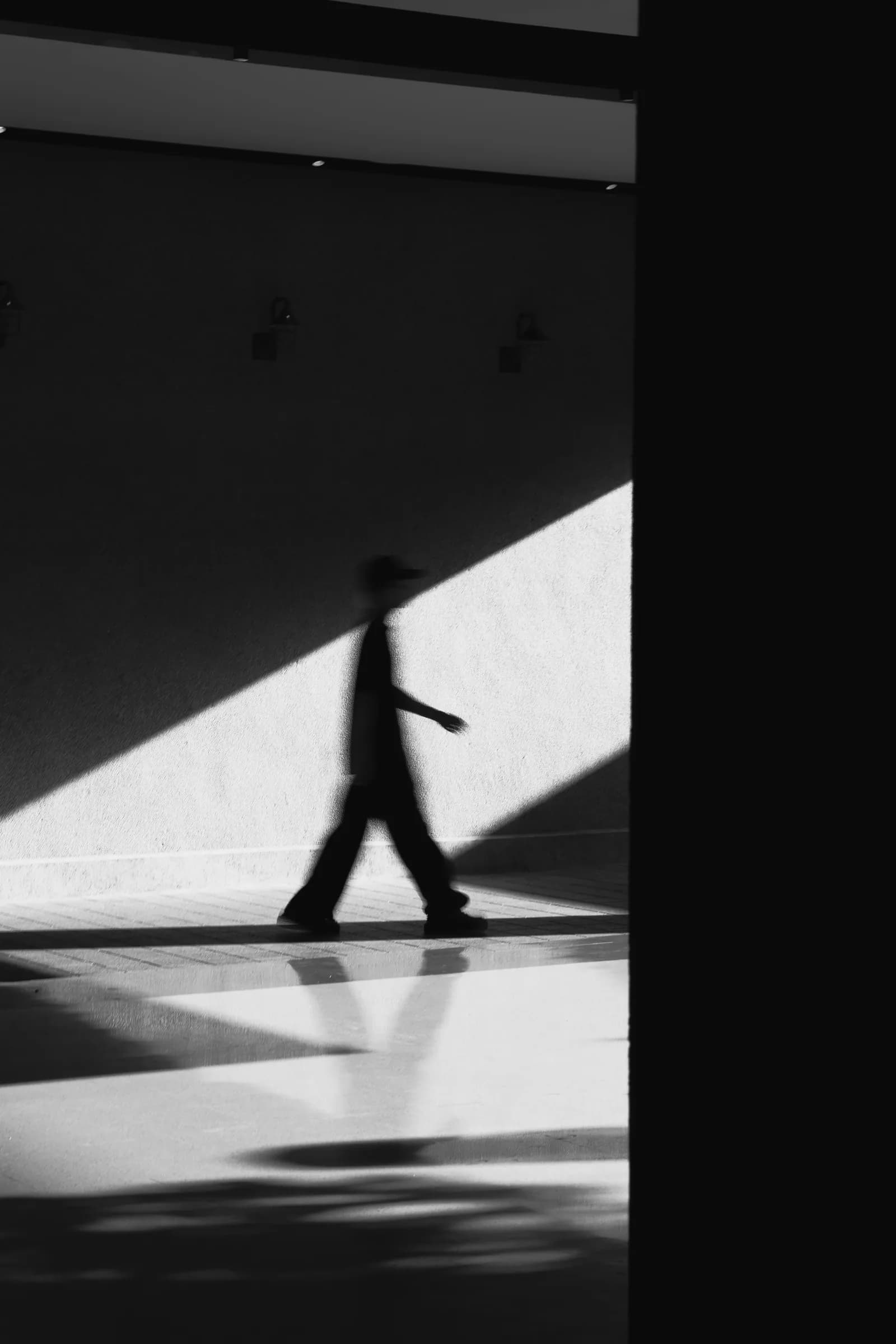A lone figure walking past a sunlit wall, in high-contrast monochrome