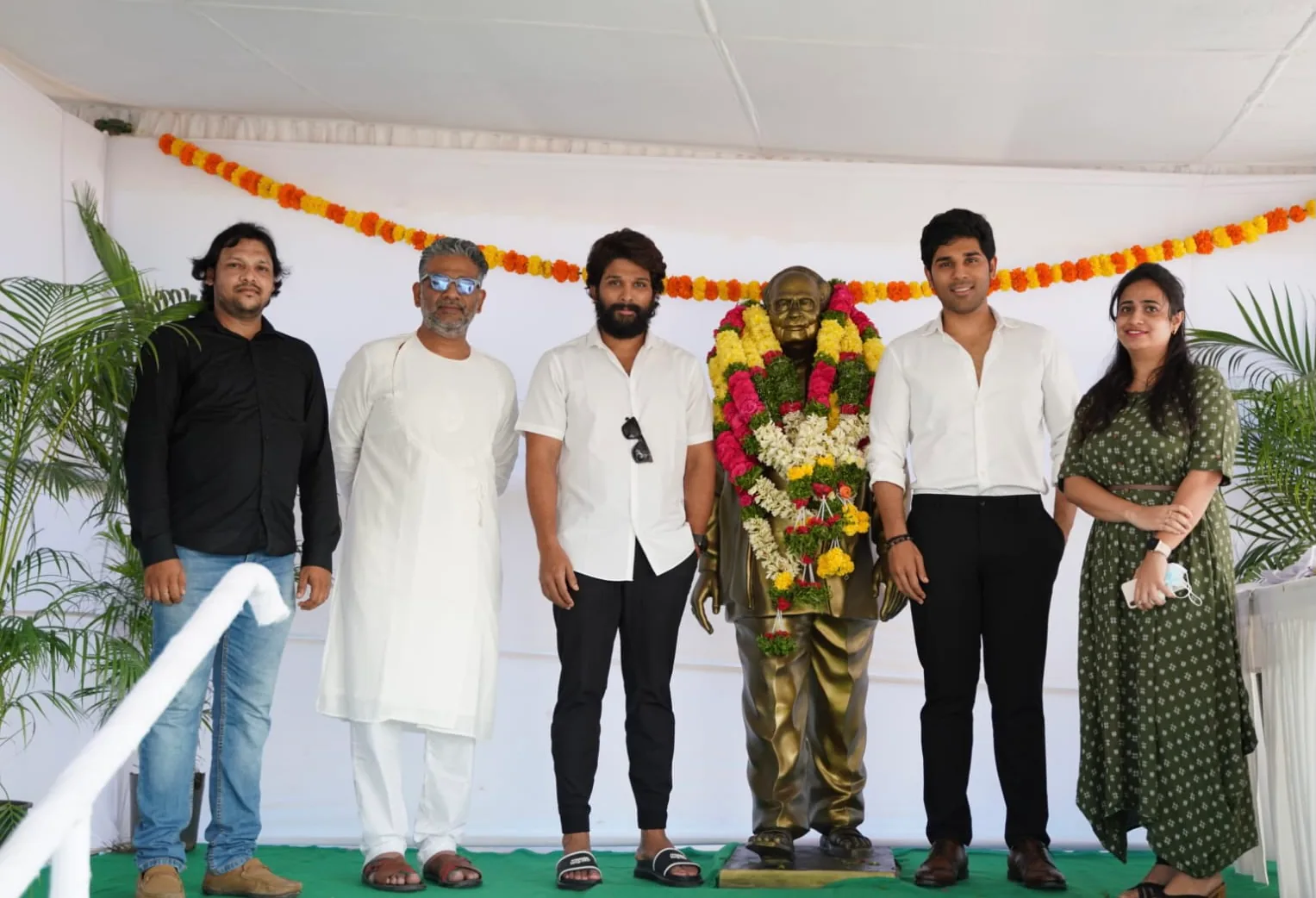 A group standing beside a garlanded bronze statue beneath a white canopy at the unveiling