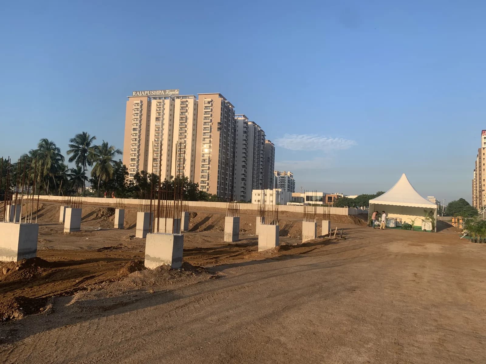 A cleared site with foundation piers laid out, apartment towers beyond