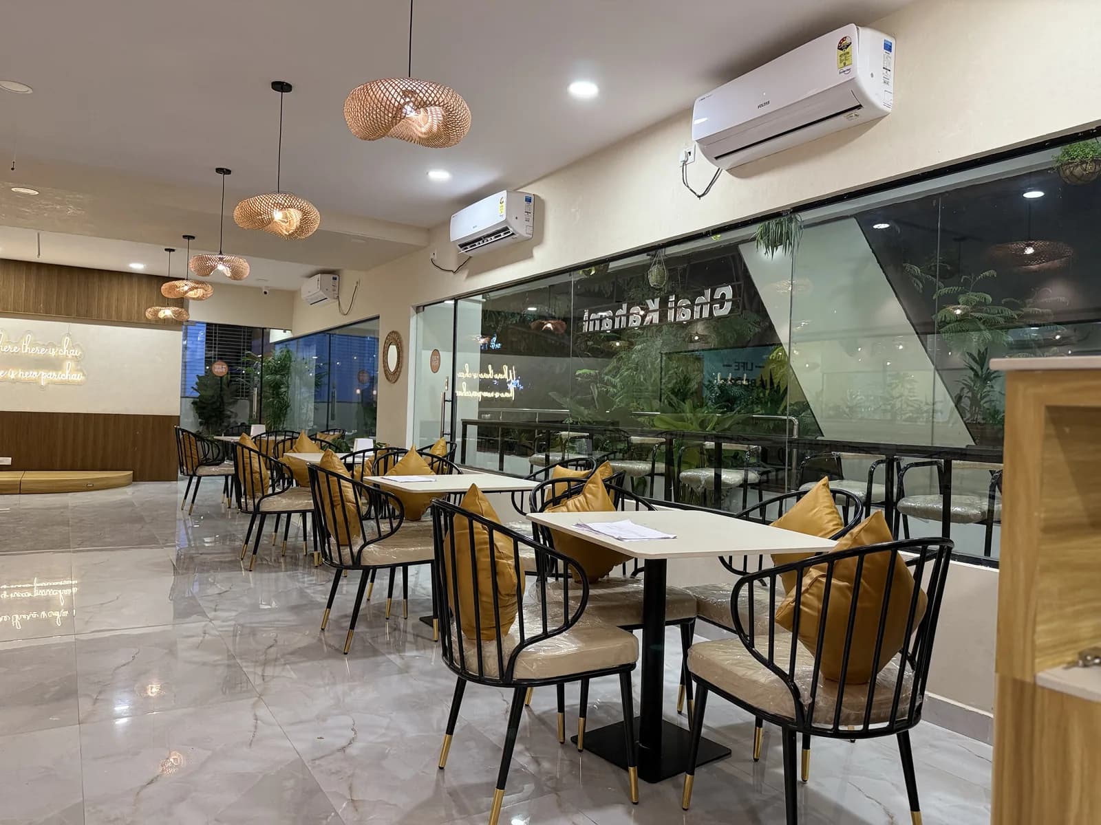 A café floor with woven pendants above pale tables and black cane chairs
