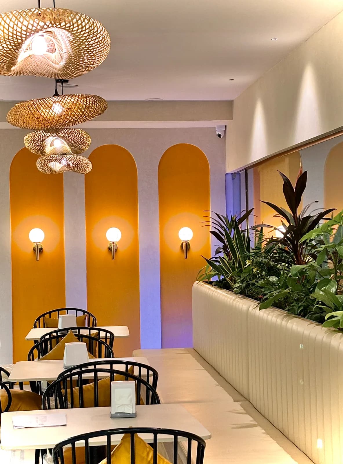 A row of ochre arches with wall sconces, above a pale banquette and planting