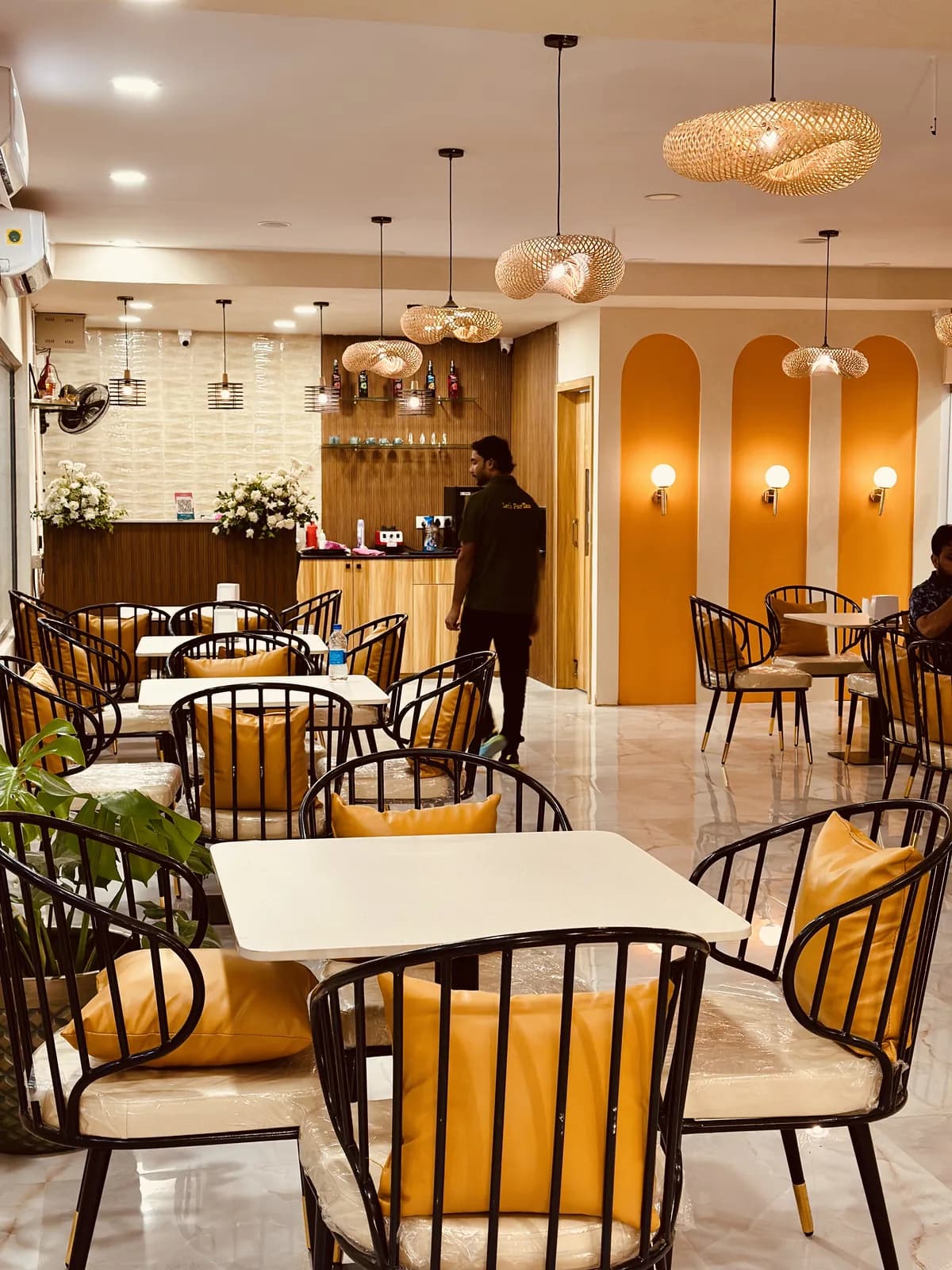 A cafe floor with cane pendants above arched niches and mustard-cushioned chairs