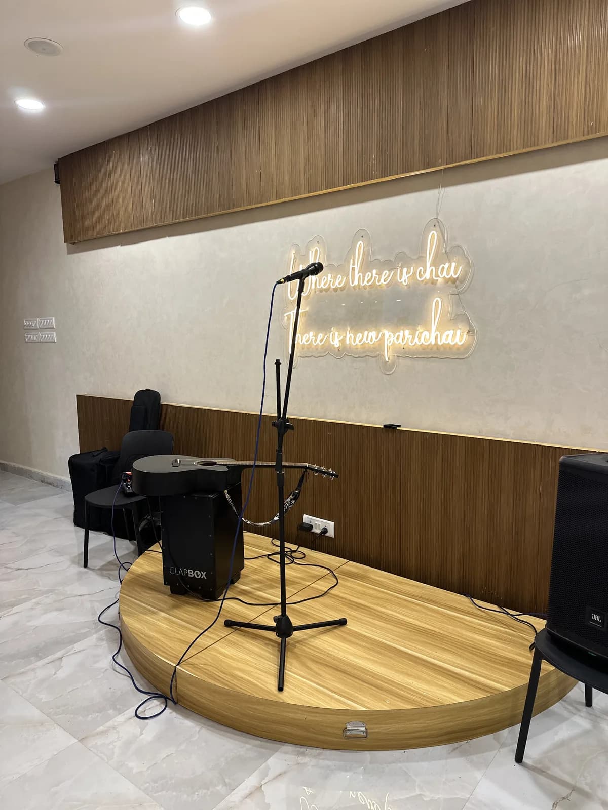 A small timber stage with a microphone below a neon script sign