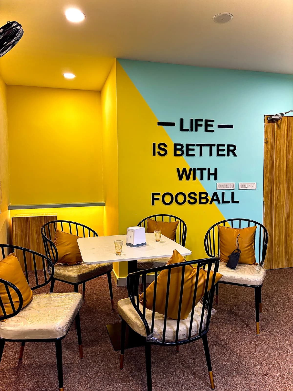 Seating beside a yellow and mint wall carrying a foosball graphic