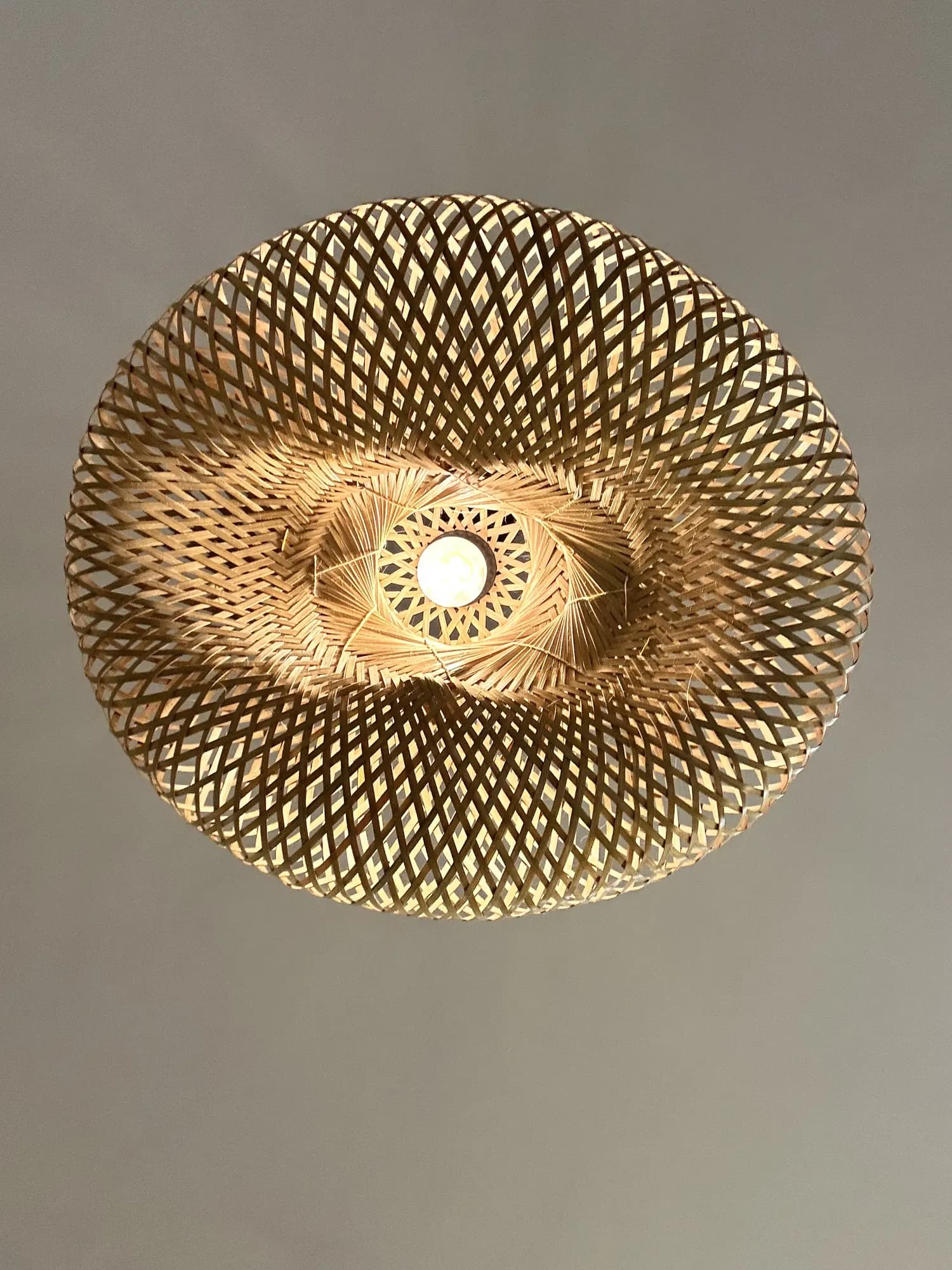 A large woven rattan pendant shade lit from within, seen from below