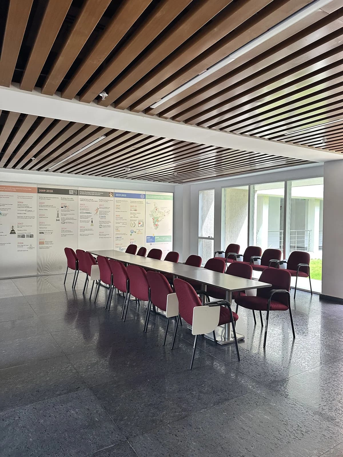 A seminar room of long tables and red chairs under a battened timber ceiling
