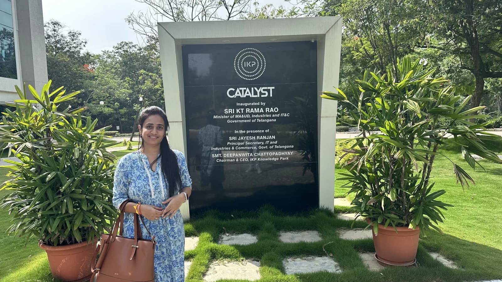 The Catalyst dedication plaque framed by potted palms, with a visitor standing beside it