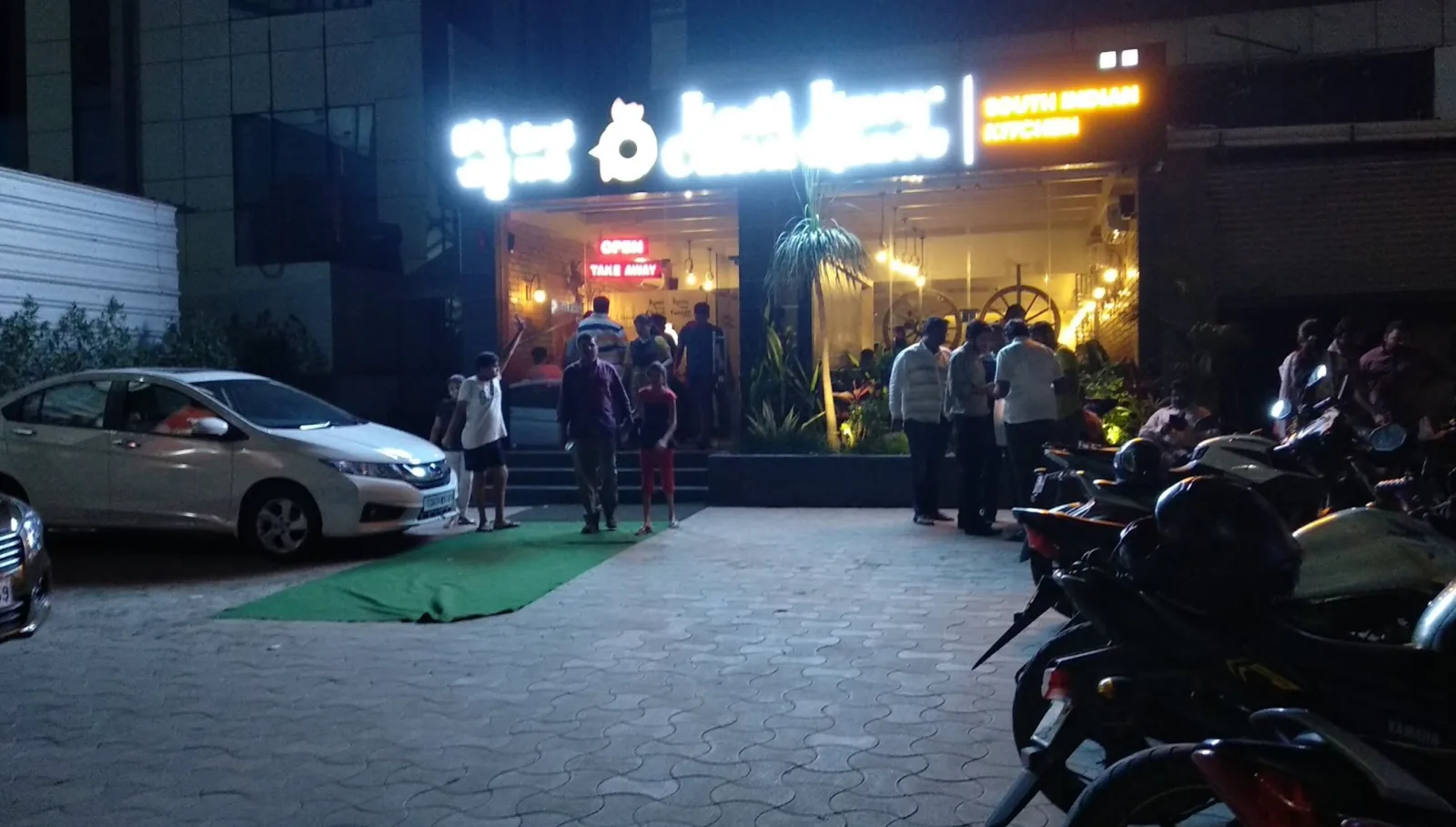 The restaurant shopfront at night with its sign lit above the forecourt