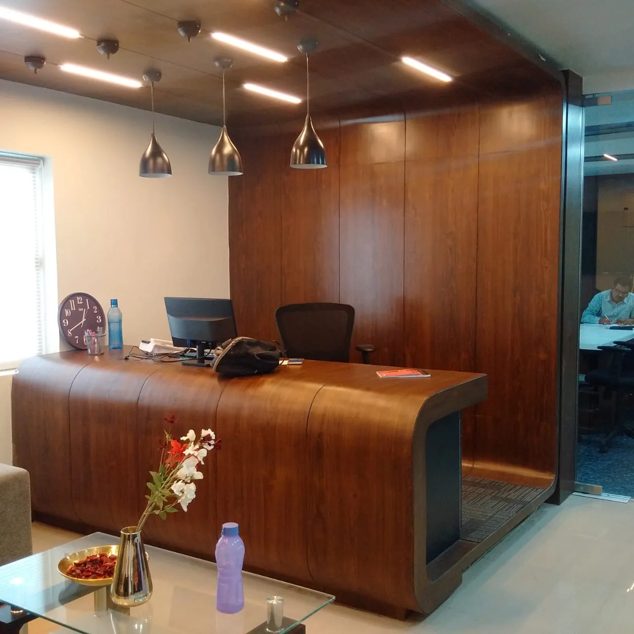 A curved walnut manager desk against a full-height timber wall