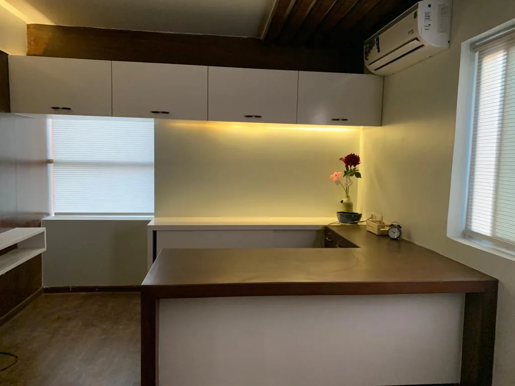 A manager's desk beneath fitted overhead cabinets and a shaded window
