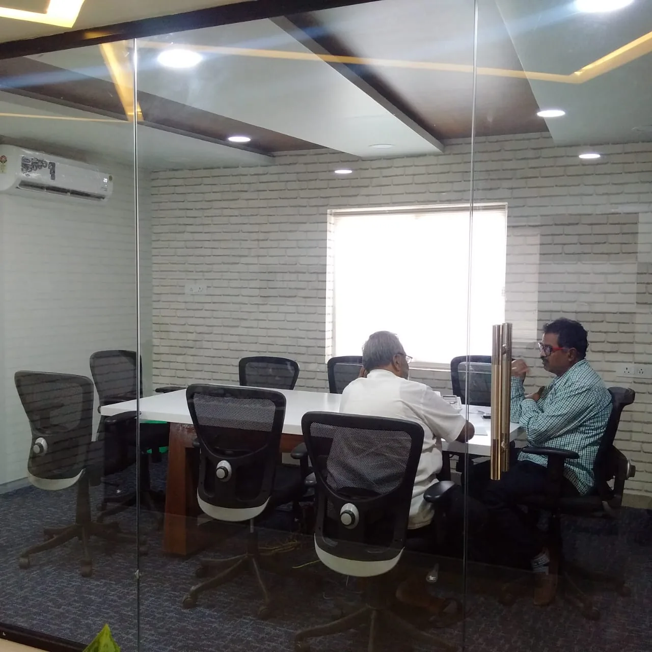 A meeting in progress behind a glazed partition, brick wall beyond