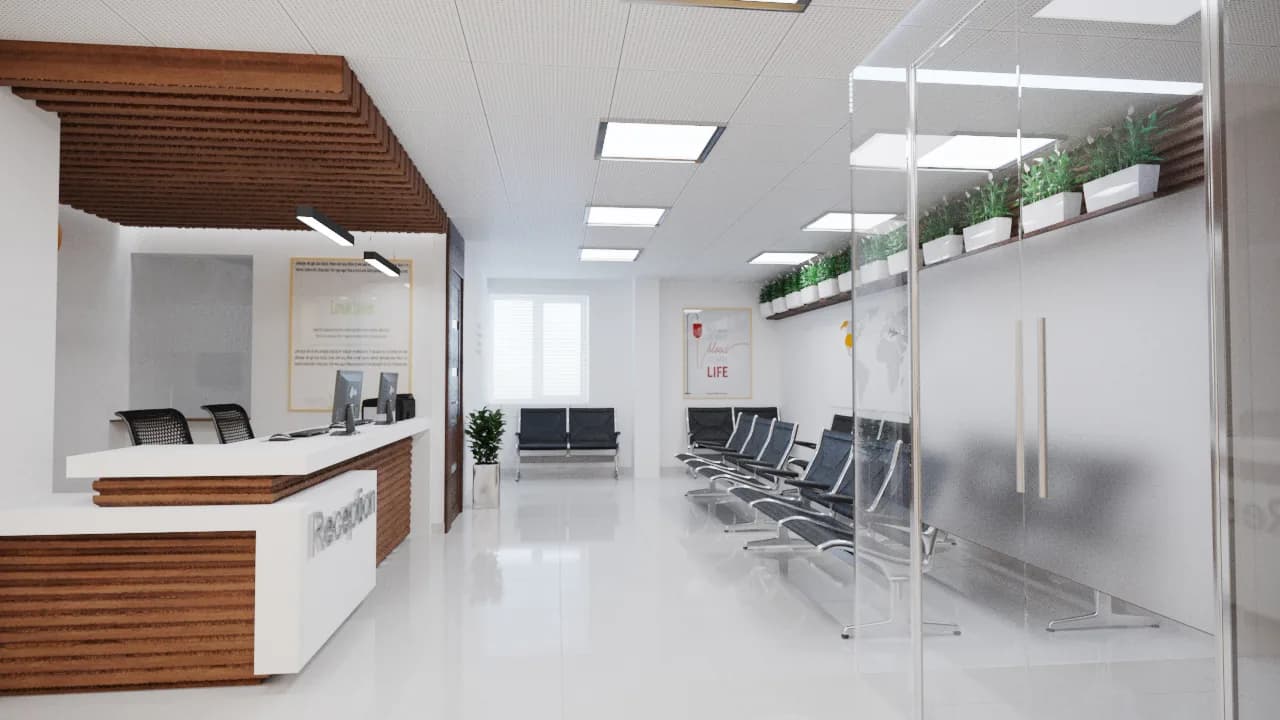 A hospital reception with a pale timber desk, a row of seats and planting on a high shelf