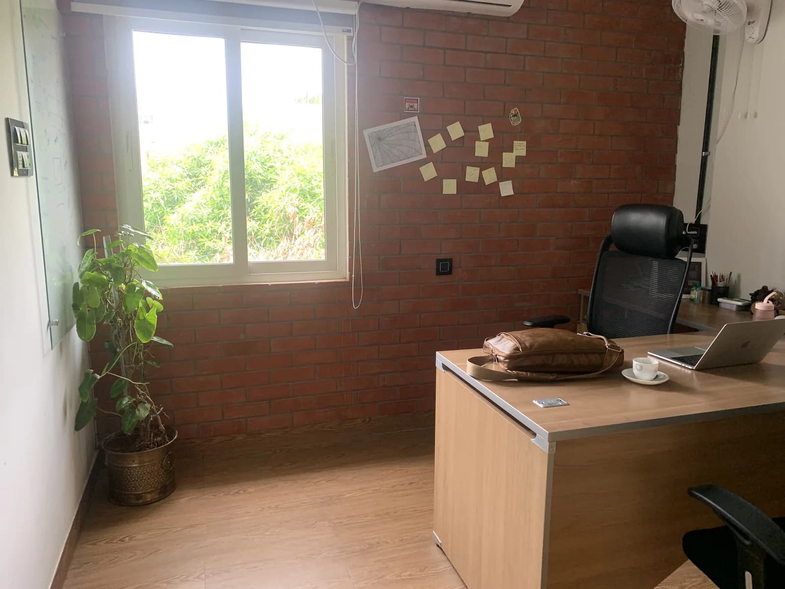 A private office with a timber desk set against exposed brick and a garden window
