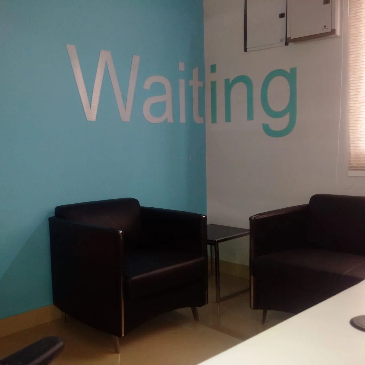 A waiting area with dark armchairs against a teal wall lettered Waiting