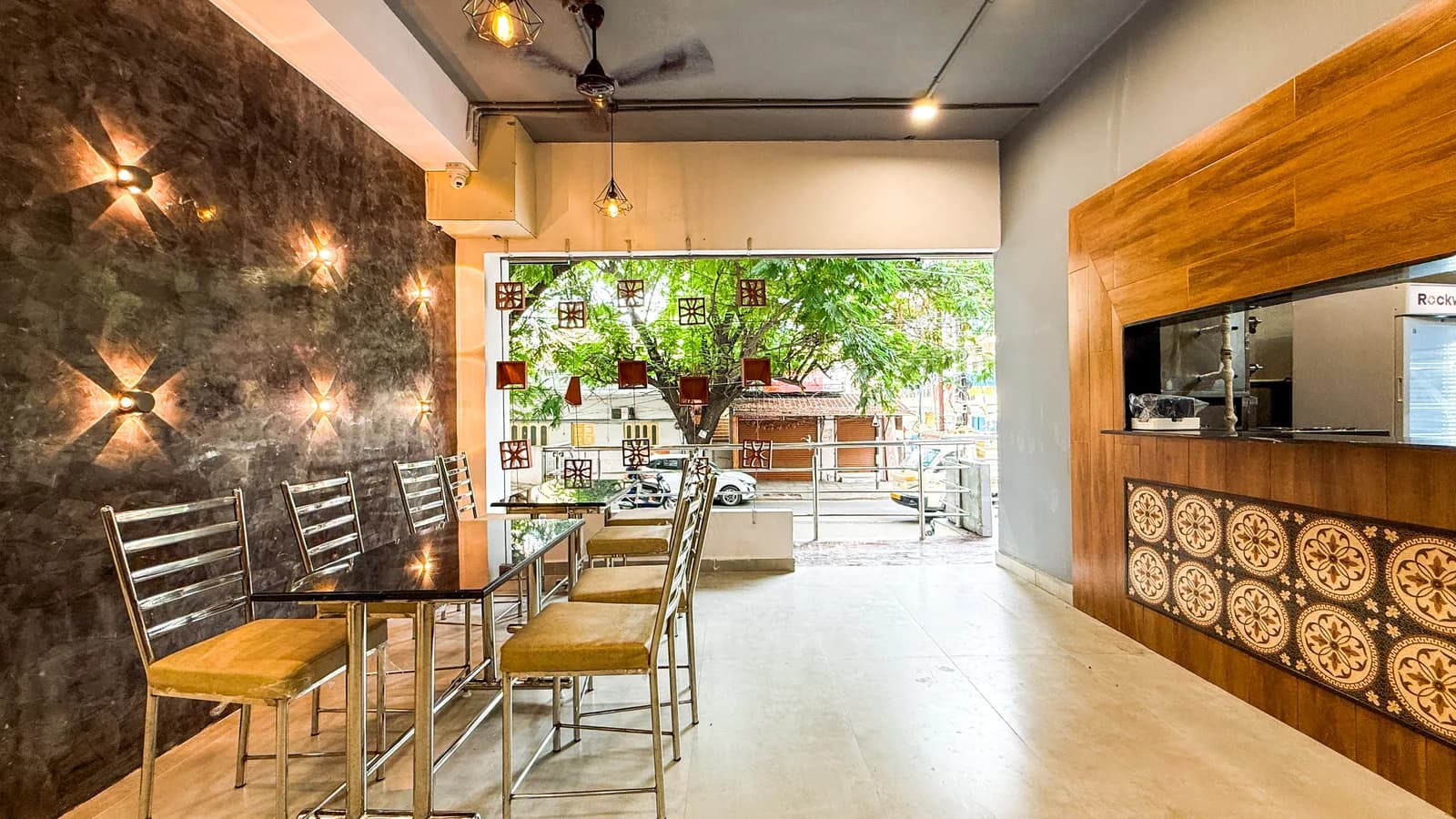 A run of counter seating facing an opening onto the street, a tree filling the view