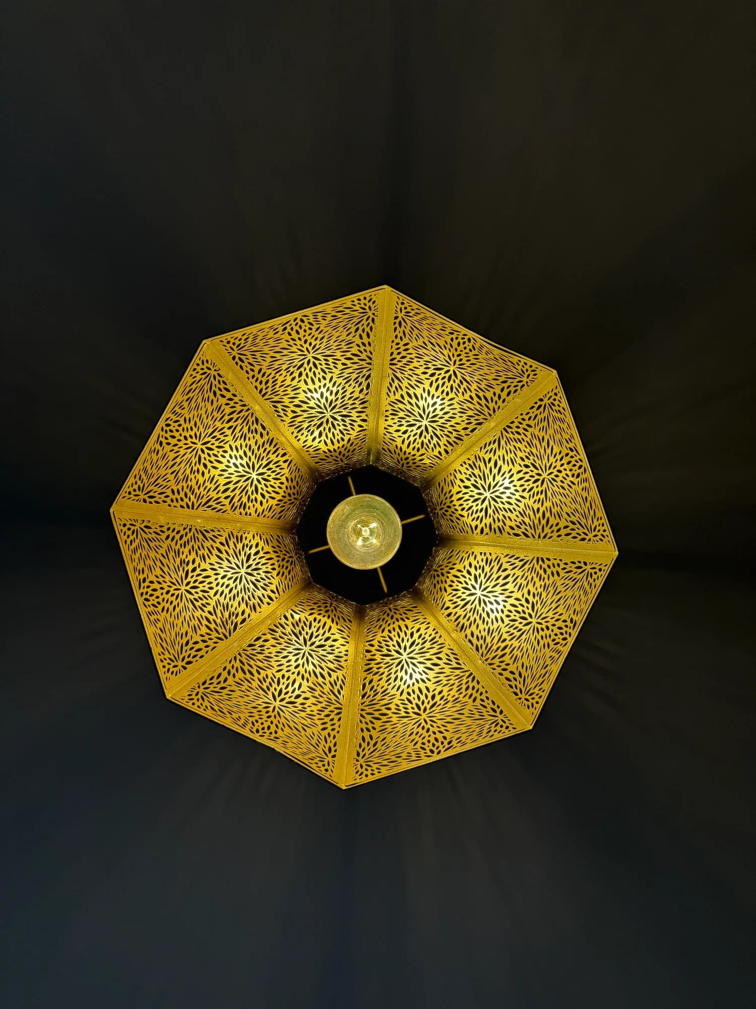A pierced brass pendant light glowing against a dark ceiling