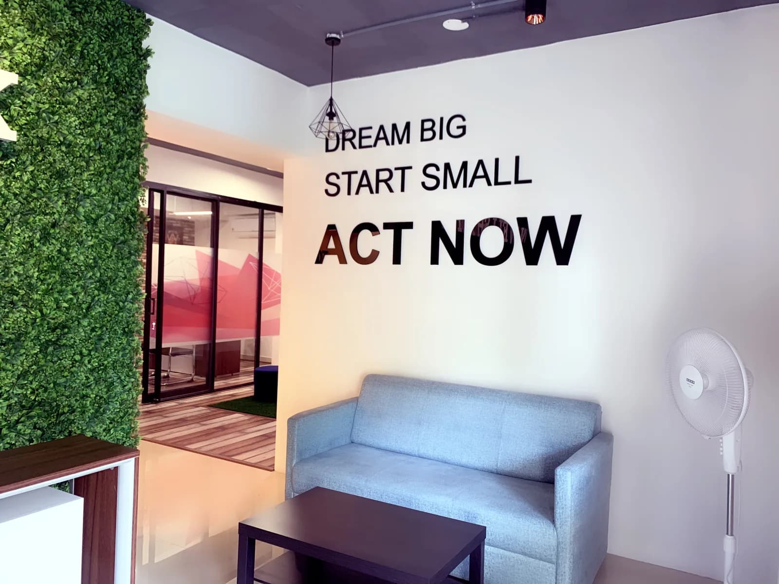 A pale blue waiting sofa below wall lettering, a glazed meeting cabin beyond