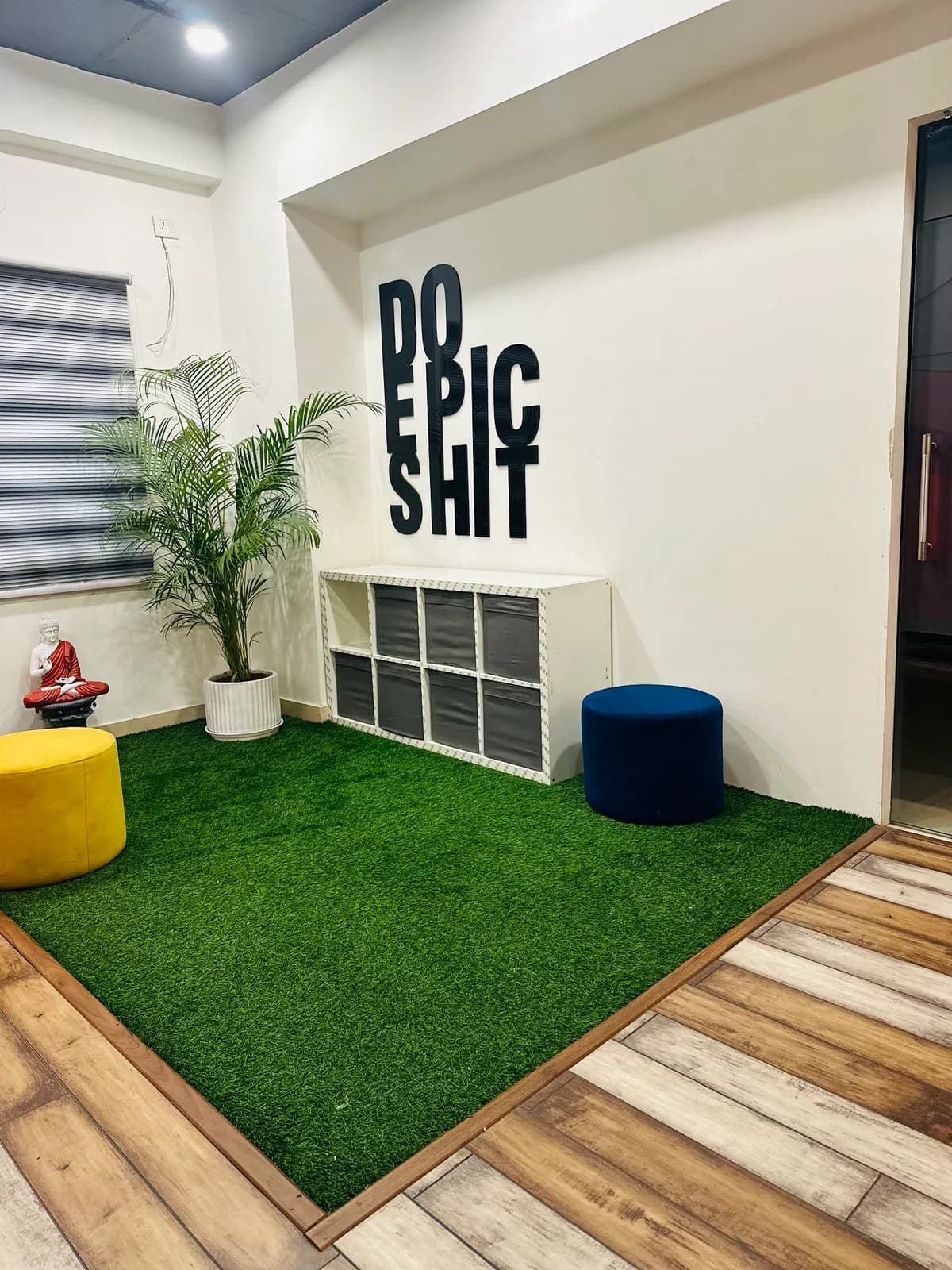 A lawn-floored corner with cube storage, a stool and a potted palm