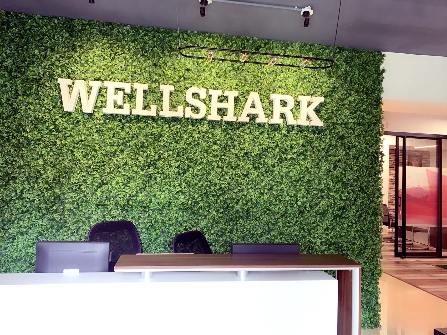 A white reception desk against a dense planted green wall carrying the company name